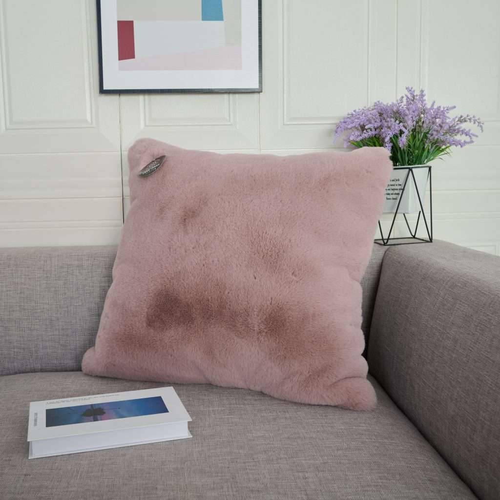 Pink fluffy cushion on grey sofa with book.
