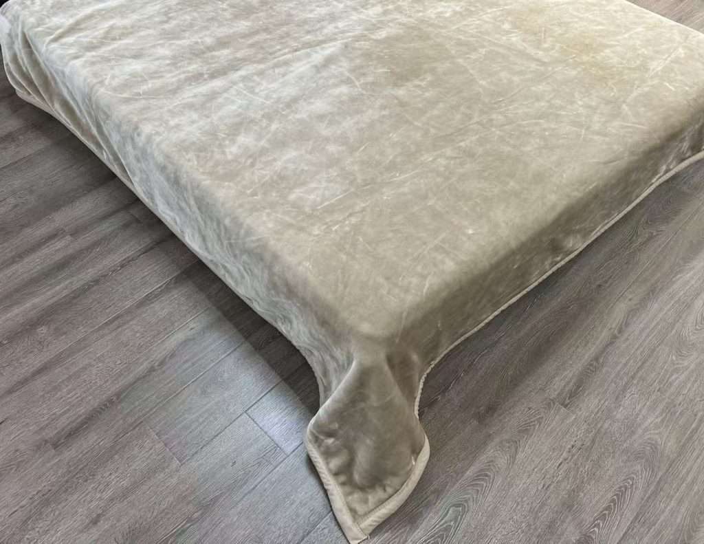 Bed with beige cover on wooden floor